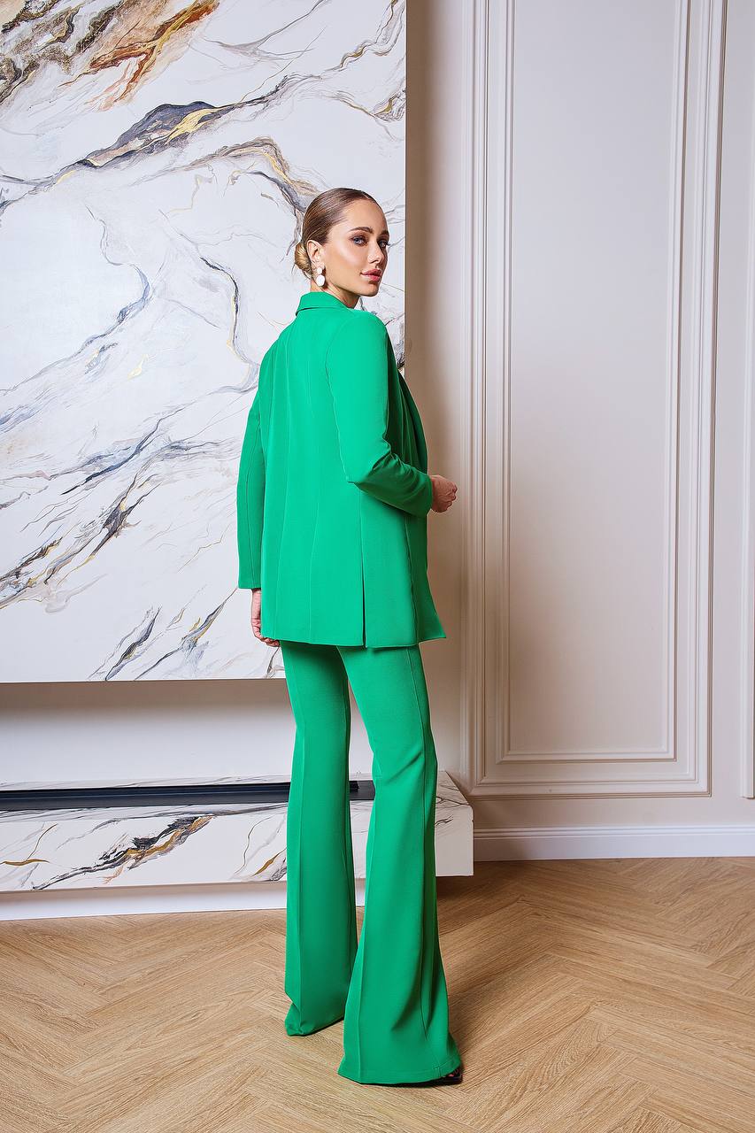 Person wearing a green suit standing in a room with marble wall and wooden floor.