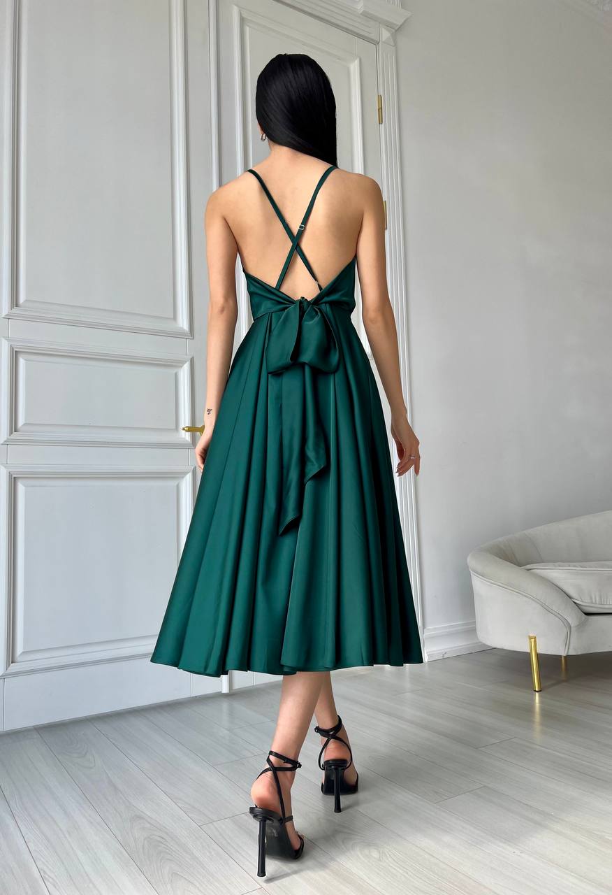 Woman wearing a green dress with a bow detail in a minimalistic room.