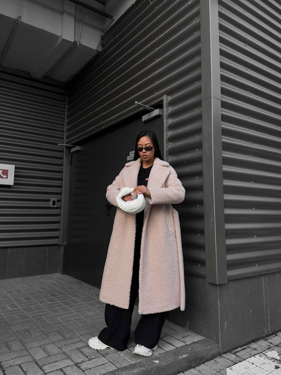 Person wearing a long pink coat standing against a dark wall.