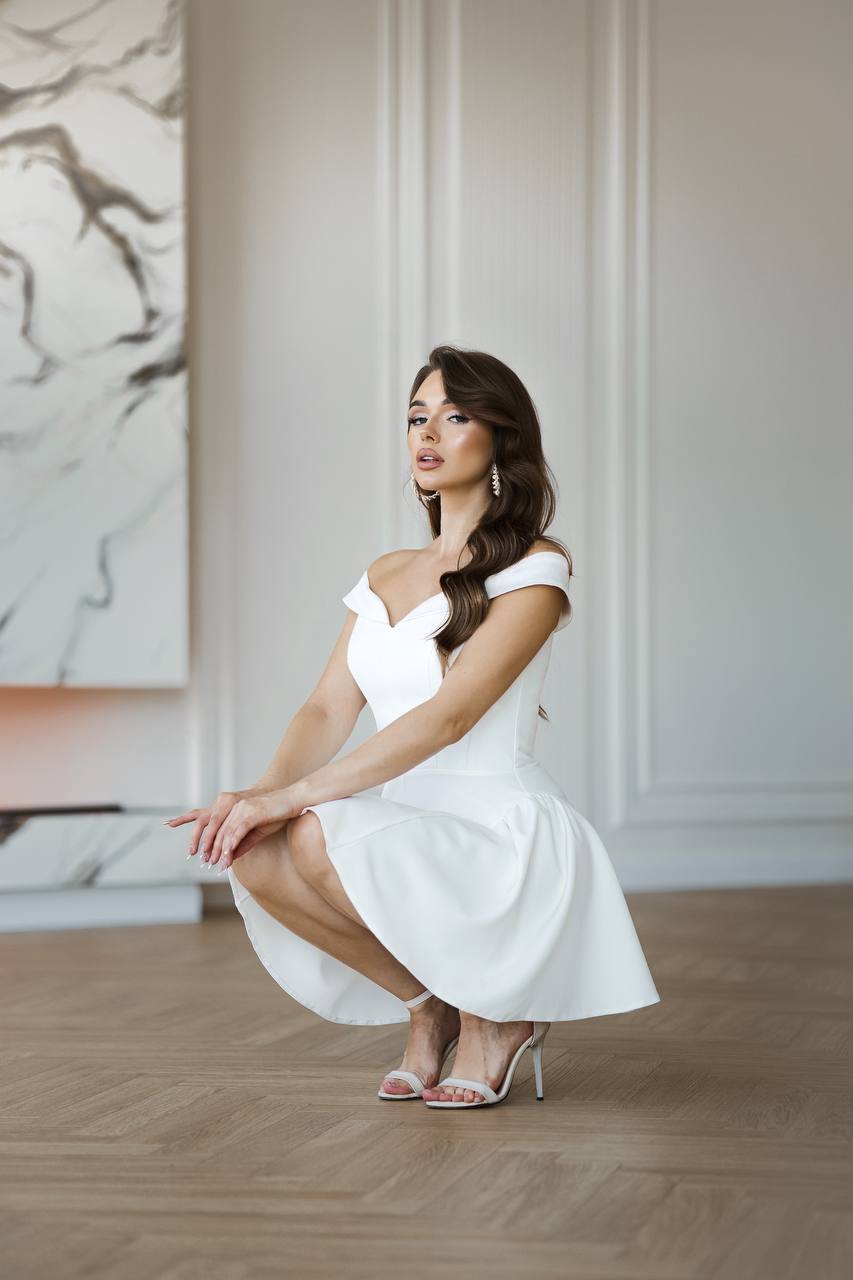 Woman in a white dress sitting on a wooden floor with a neutral wall and marble art in the background