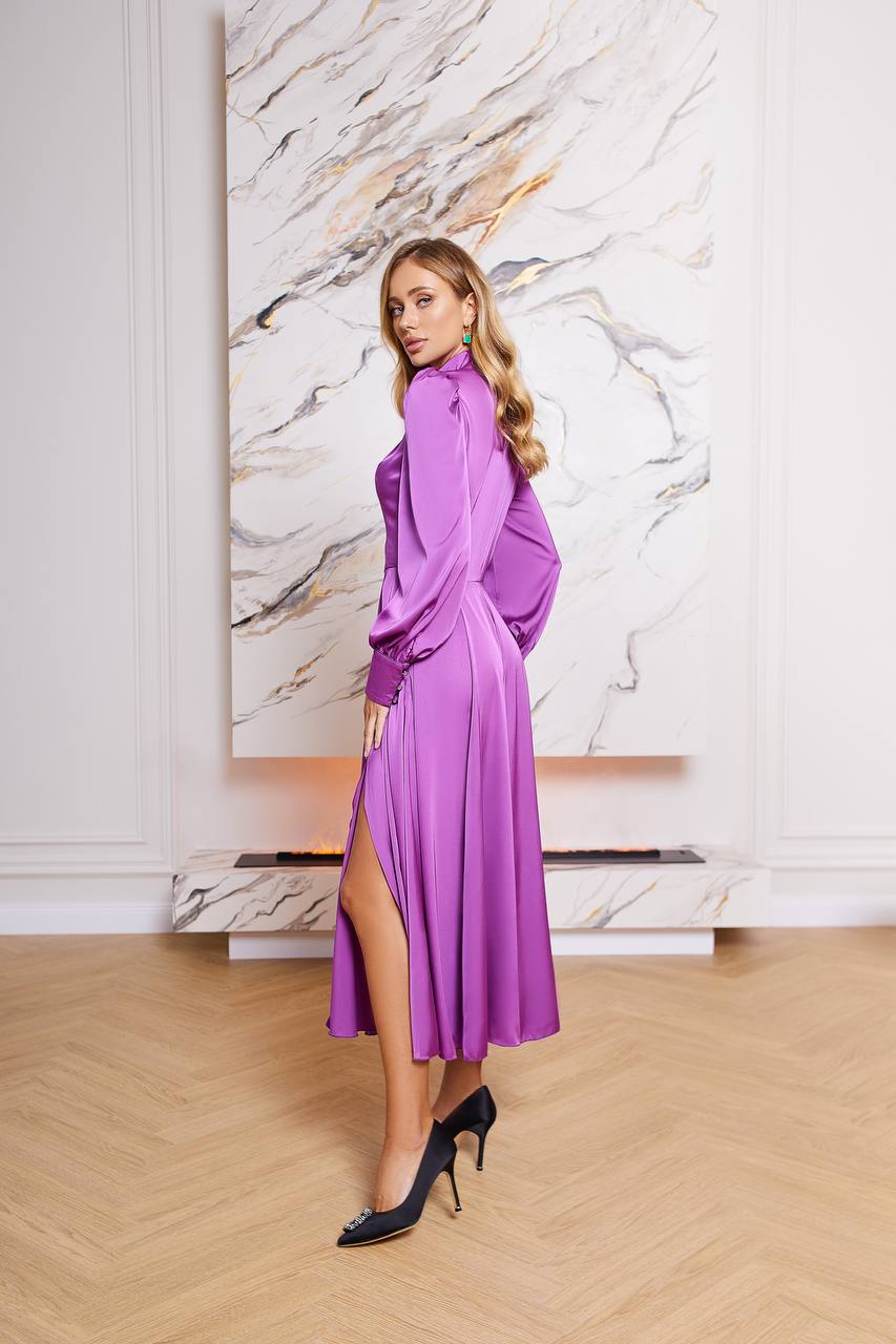 Woman in a purple dress standing in a room with a marble wall.