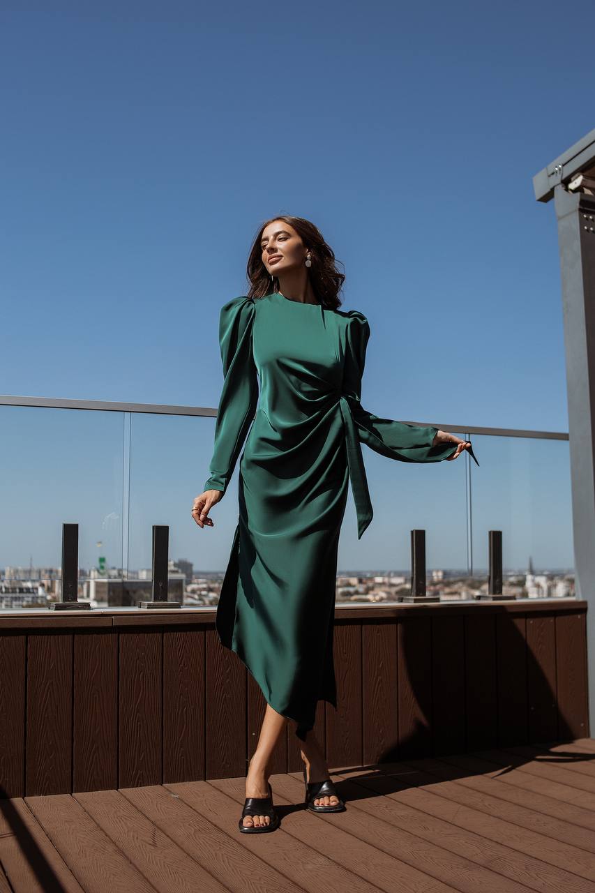 Woman in a green dress standing on a rooftop with a cityscape in the background
