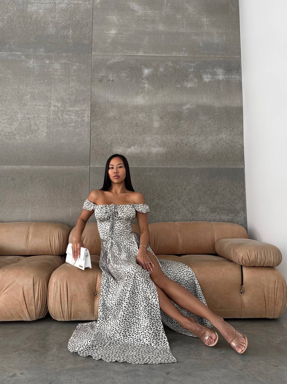 Woman in a silver off-shoulder dress sitting on a brown sofa against a gray wall.
