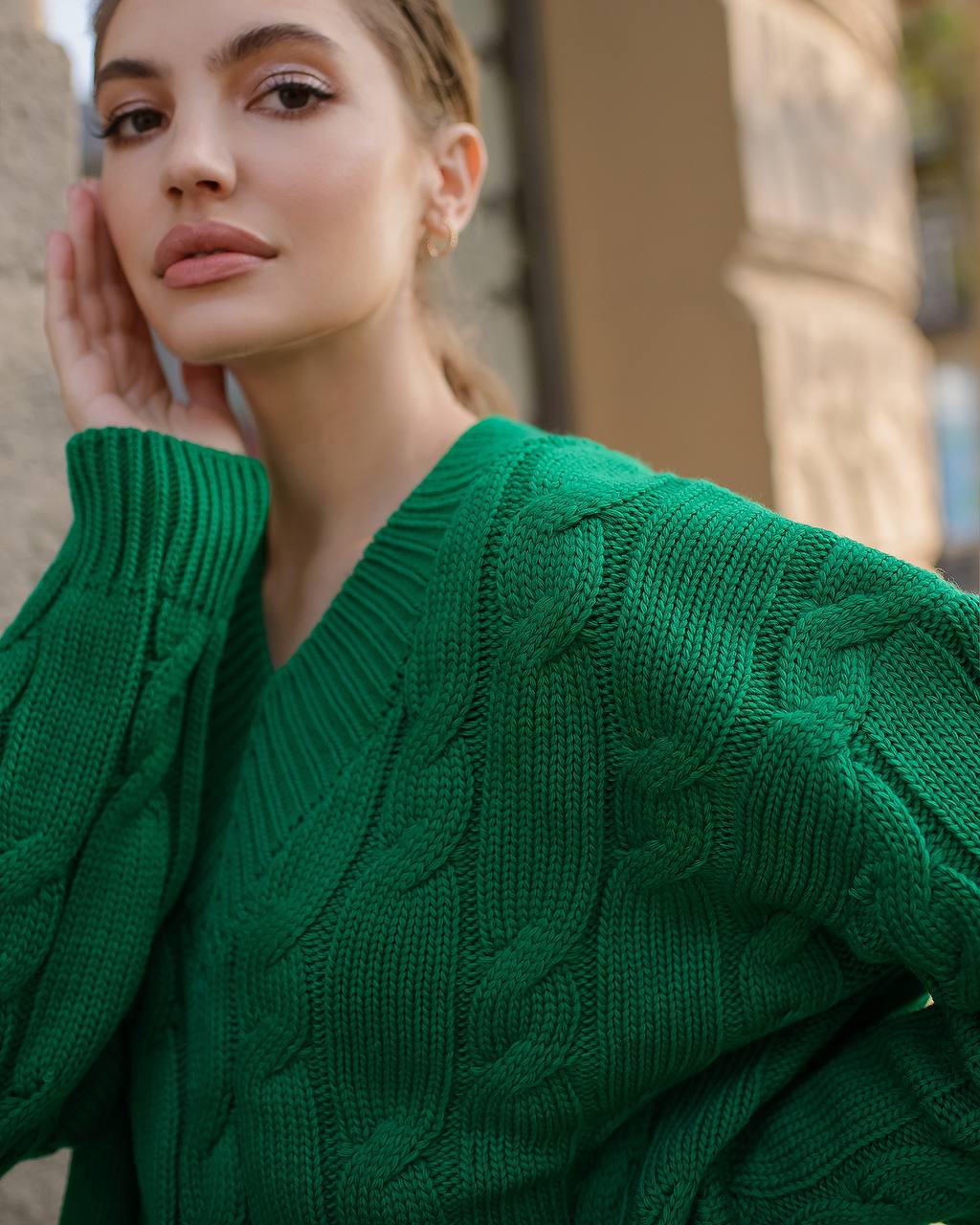 Woman wearing a green cable knit sweater with a blurred background