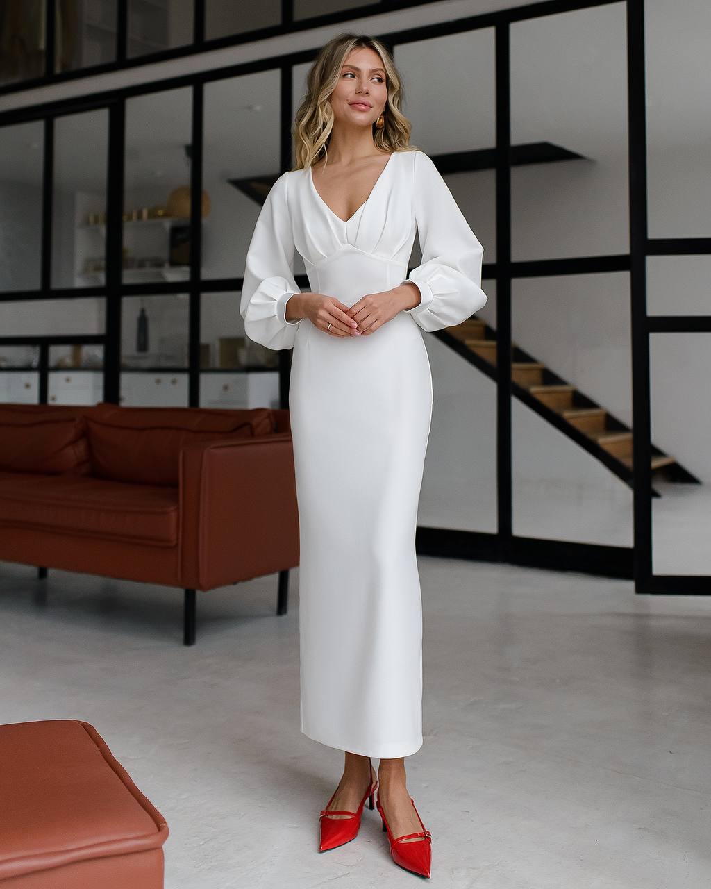 Woman in a white dress with red shoes standing in a modern interior setting.