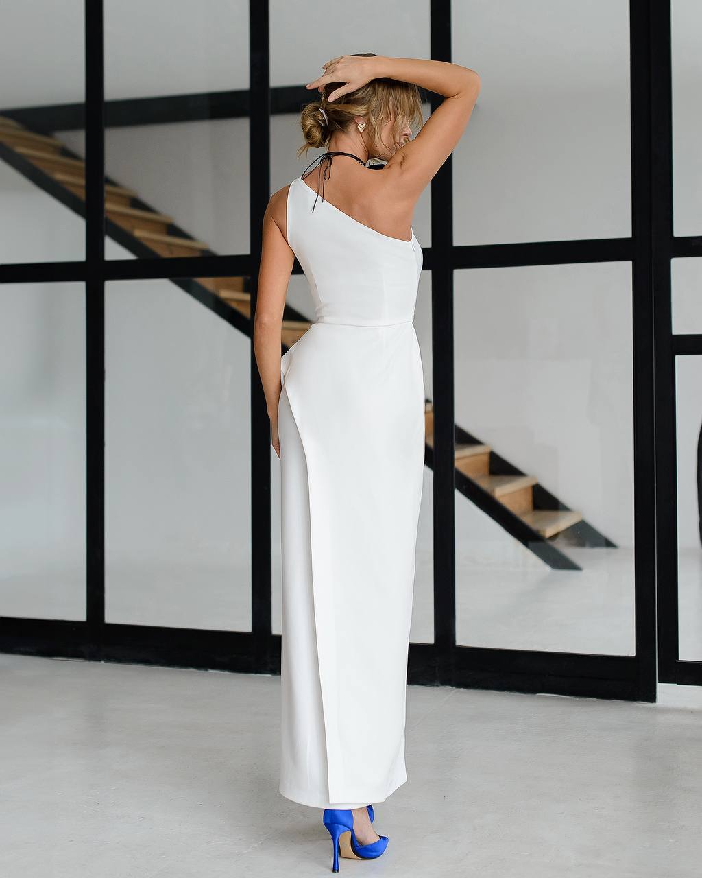 Woman in a white dress standing in a modern interior setting with a staircase.