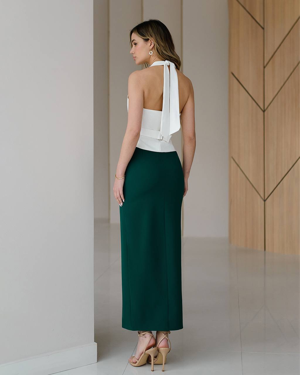 Woman wearing a white top and green skirt in a minimalistic setting