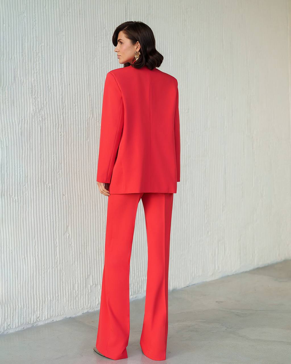 Woman wearing a red suit standing against a white wall.