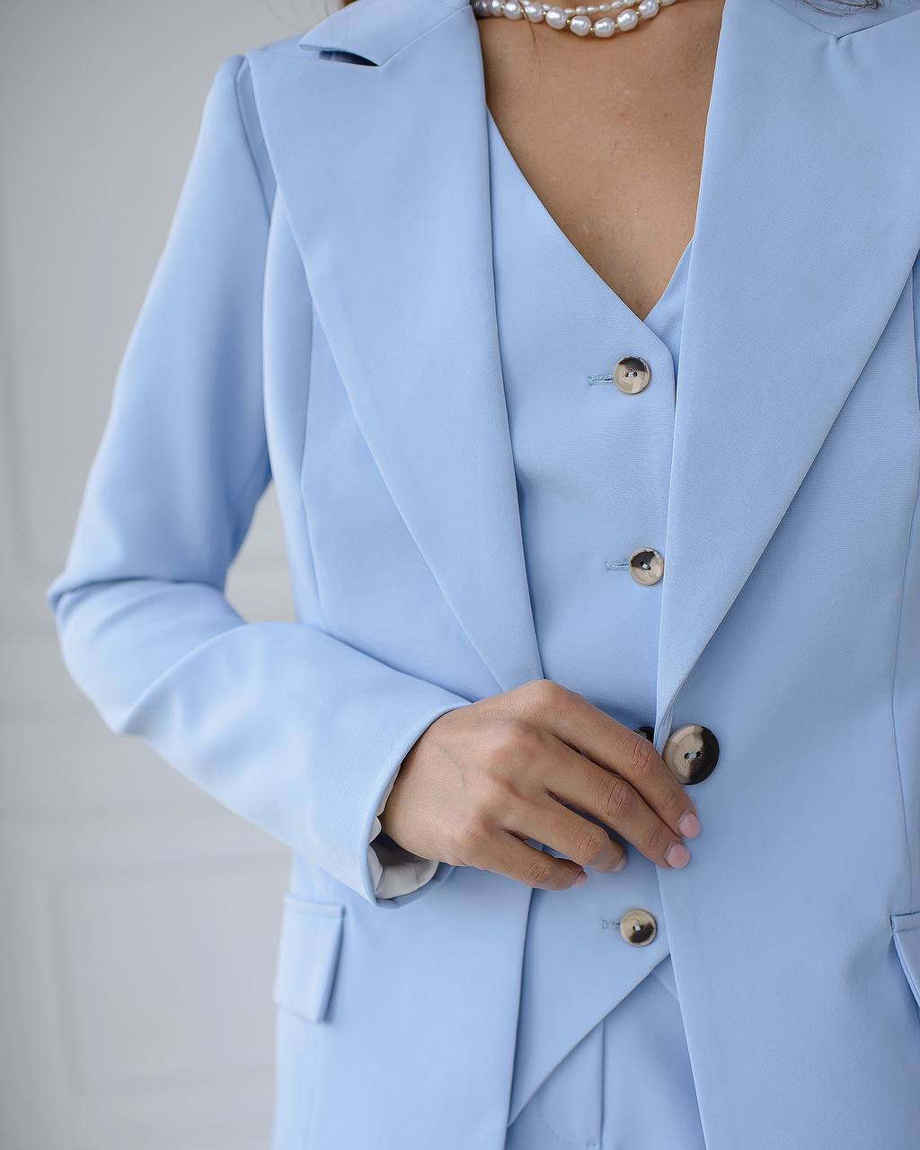 Light blue suit with pearl necklace on a neutral background