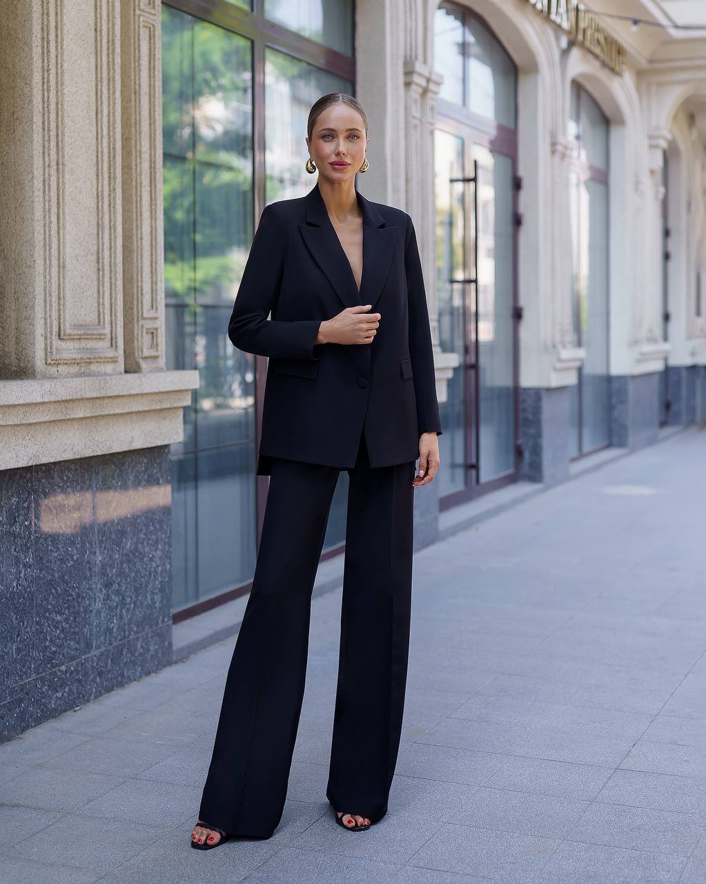 Woman in a black suit standing on a city street with classical architecture.