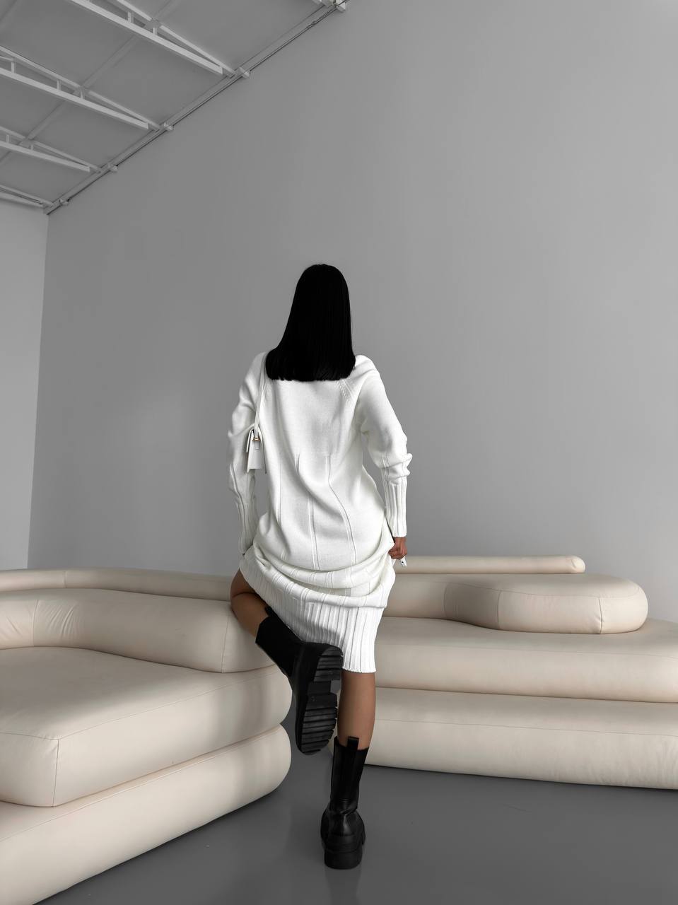 Person in a white outfit walking in a minimalistic room with gray walls and beige furniture.
