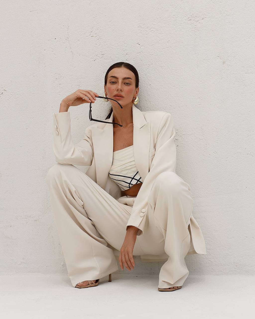 Woman in a white suit sitting against a white wall