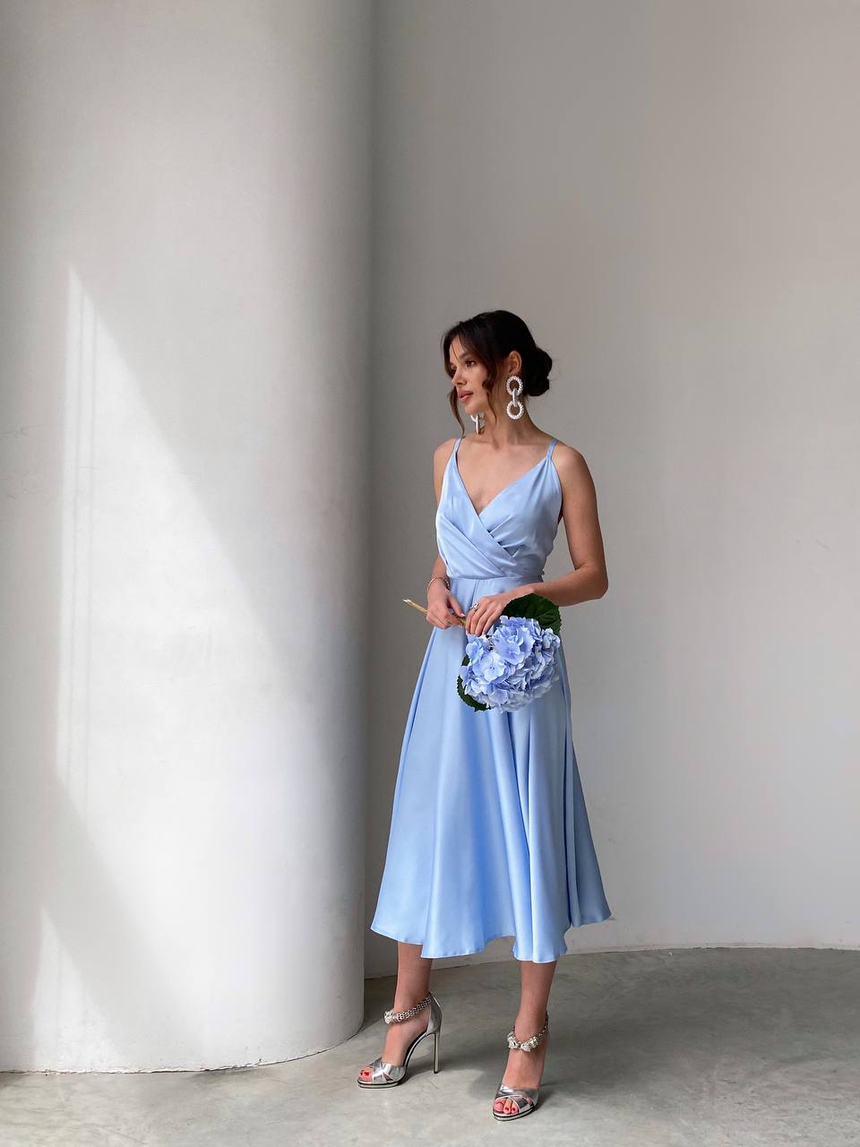 Woman in a light blue dress holding a bouquet against a plain background