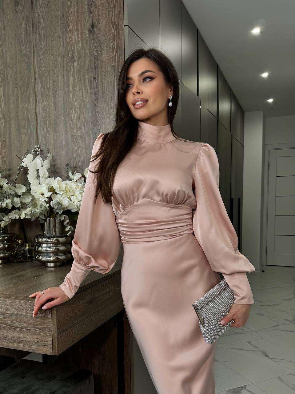 Woman in a pink satin dress holding a clutch in a modern interior setting