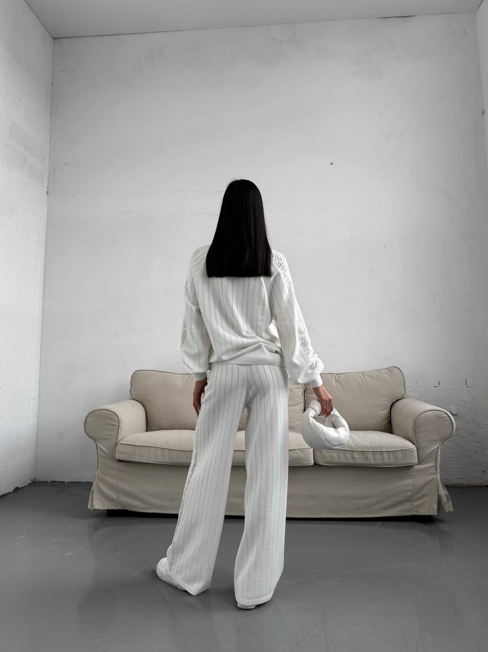 Person in a white outfit standing in a minimalistic room with a beige sofa.