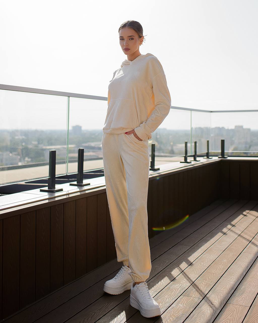 Person wearing a beige tracksuit standing on a rooftop with a cityscape view.