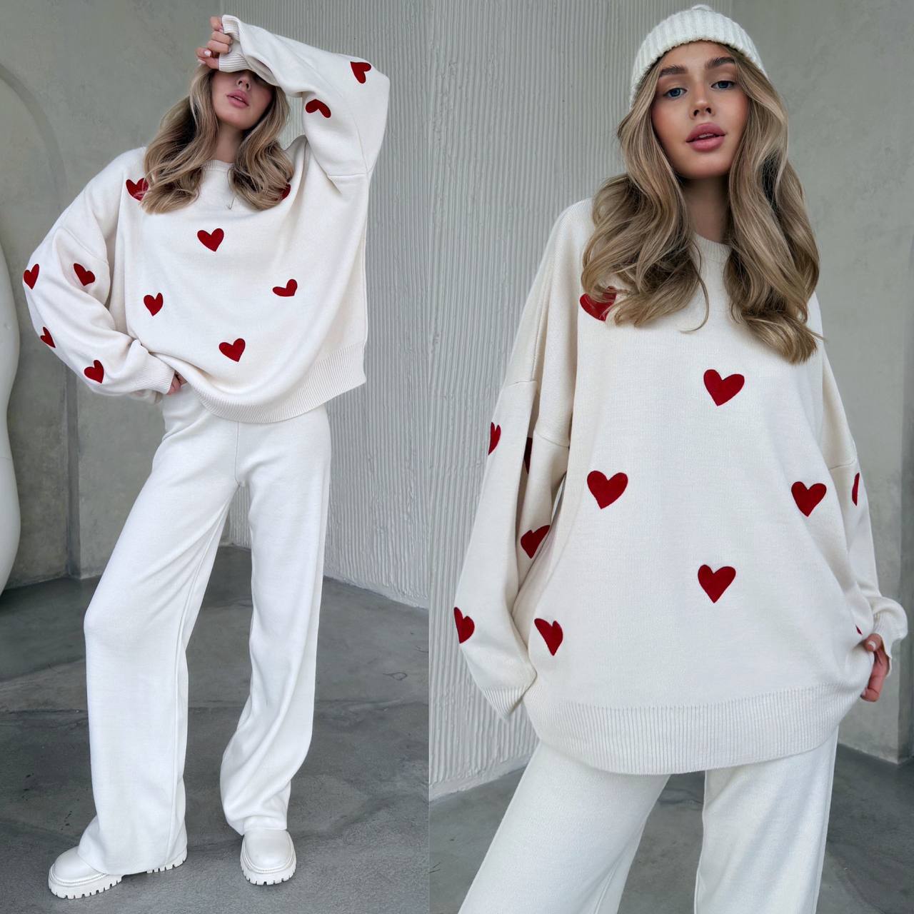 Woman wearing a white sweater with red heart patterns and white pants indoors.