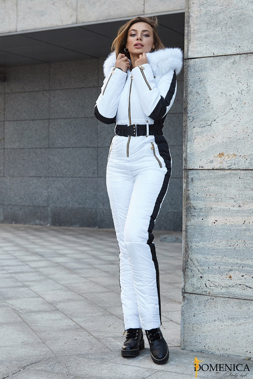Woman wearing a white snowsuit with black accents against a concrete wall.
