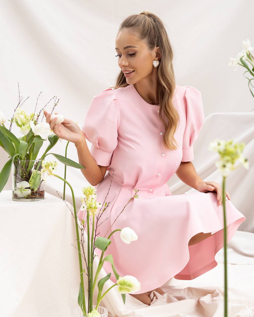 Woman in a pink dress sitting among flowers in a bright setting