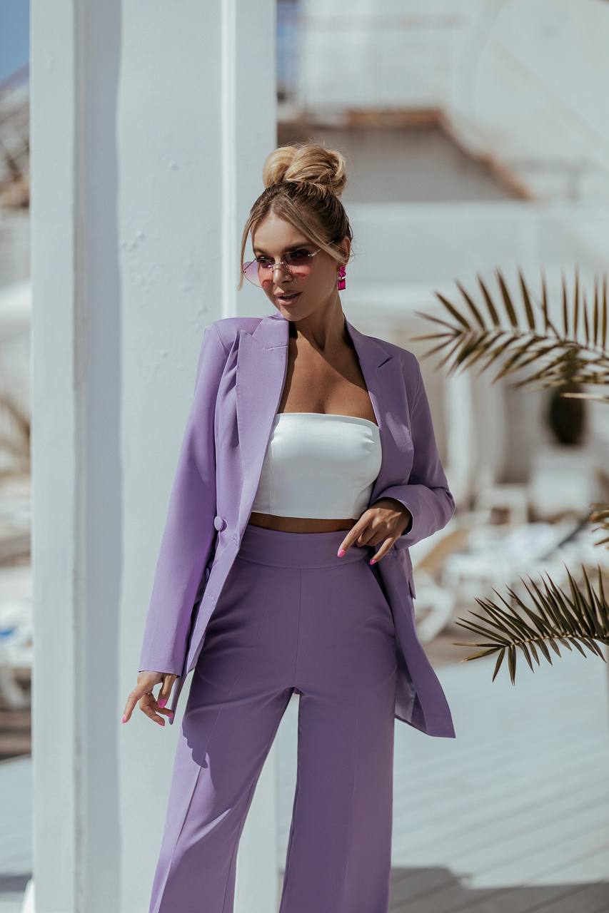 Woman in a purple suit standing outdoors with white columns and plants in the background