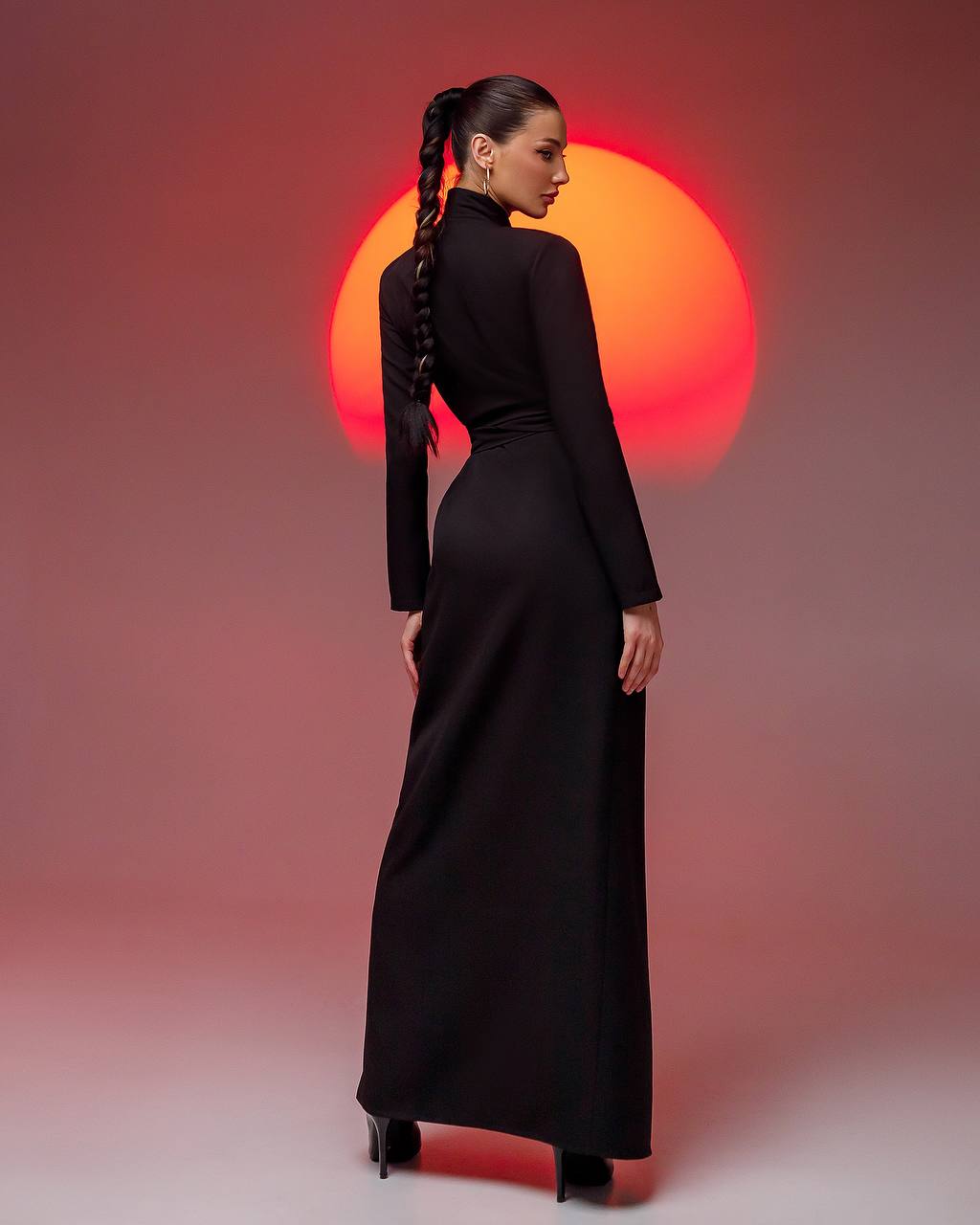 Woman in a black dress standing with her back to the camera against a warm-toned background
