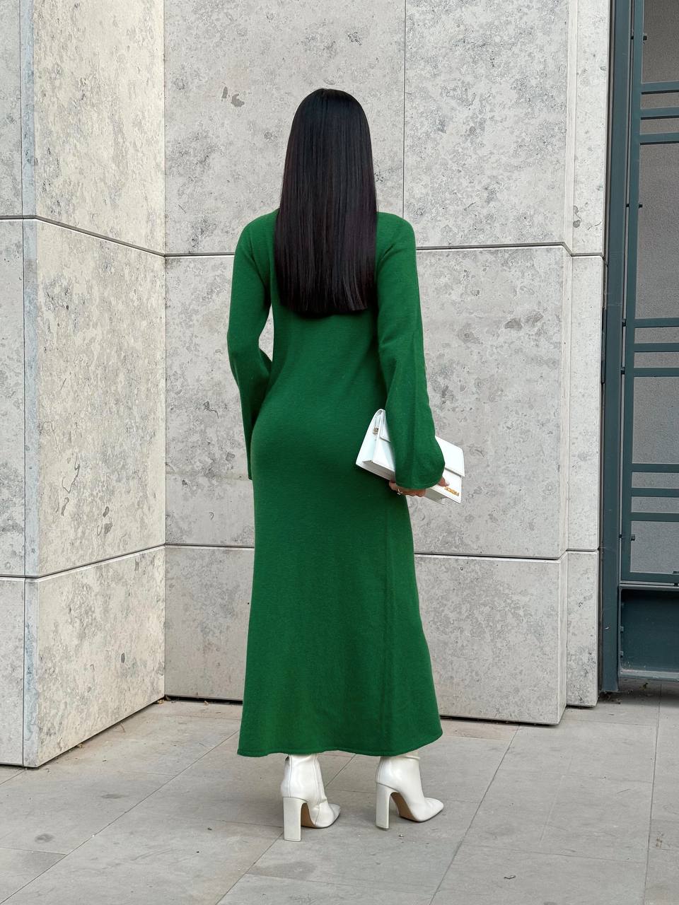 Woman in a green dress standing against a gray wall.