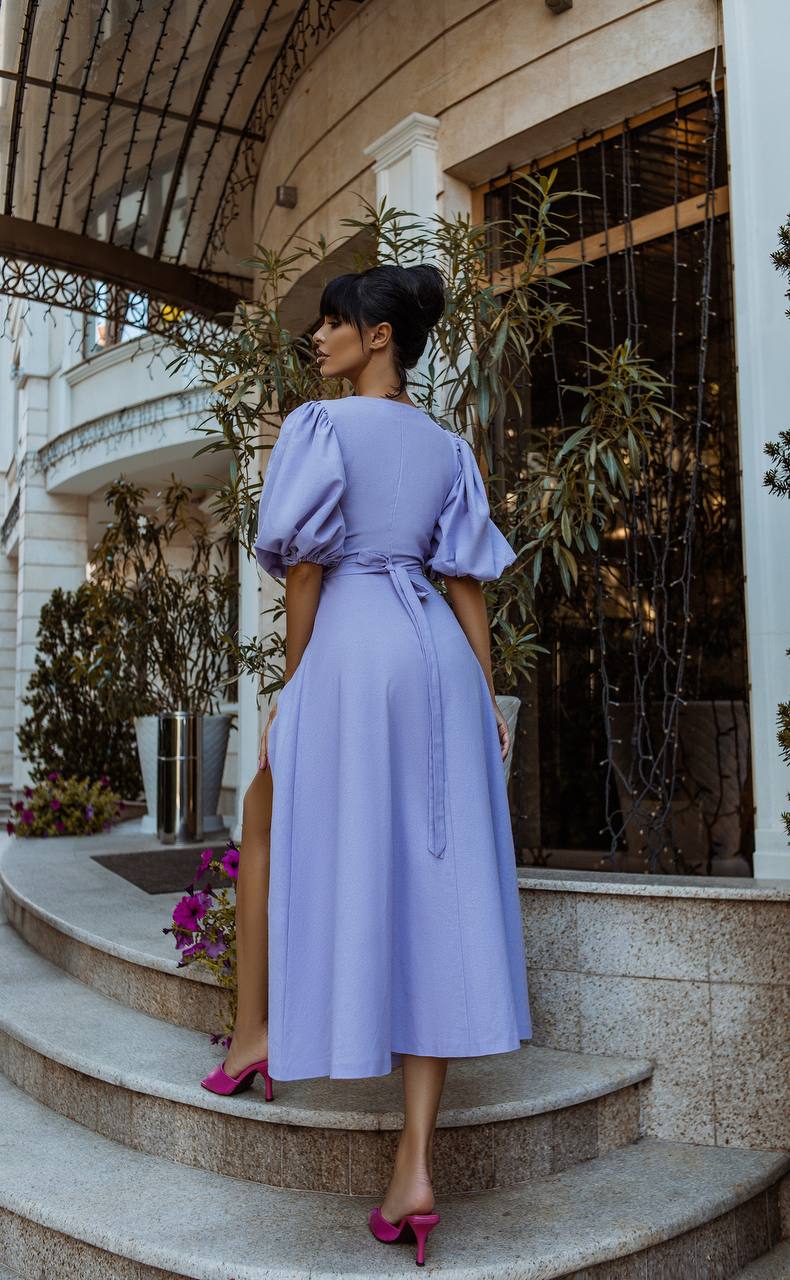 Woman in a lavender dress standing on steps with decorative plants and architecture in the background