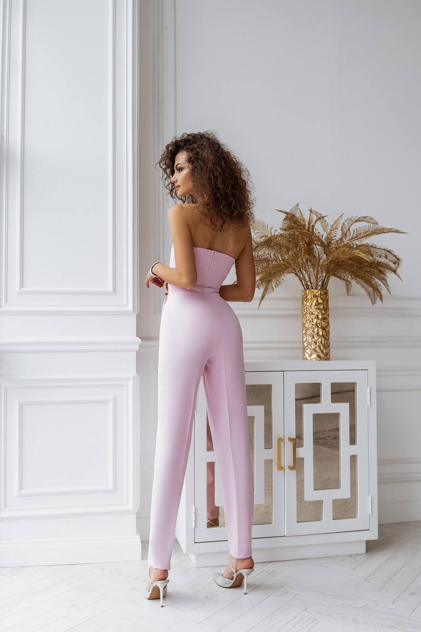 Woman in a pink strapless jumpsuit standing in a stylish room with decorative elements.