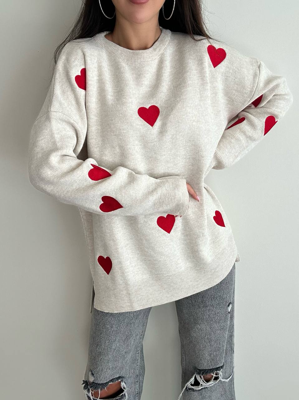 Person wearing a cream sweater with red heart patterns against a plain background