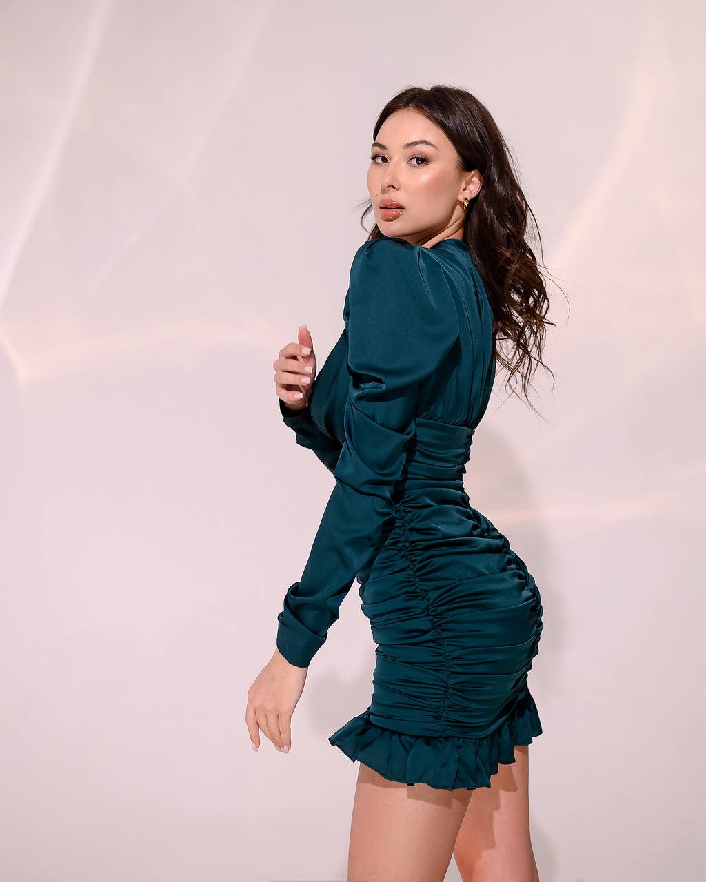 Woman wearing a teal dress against a light pink background