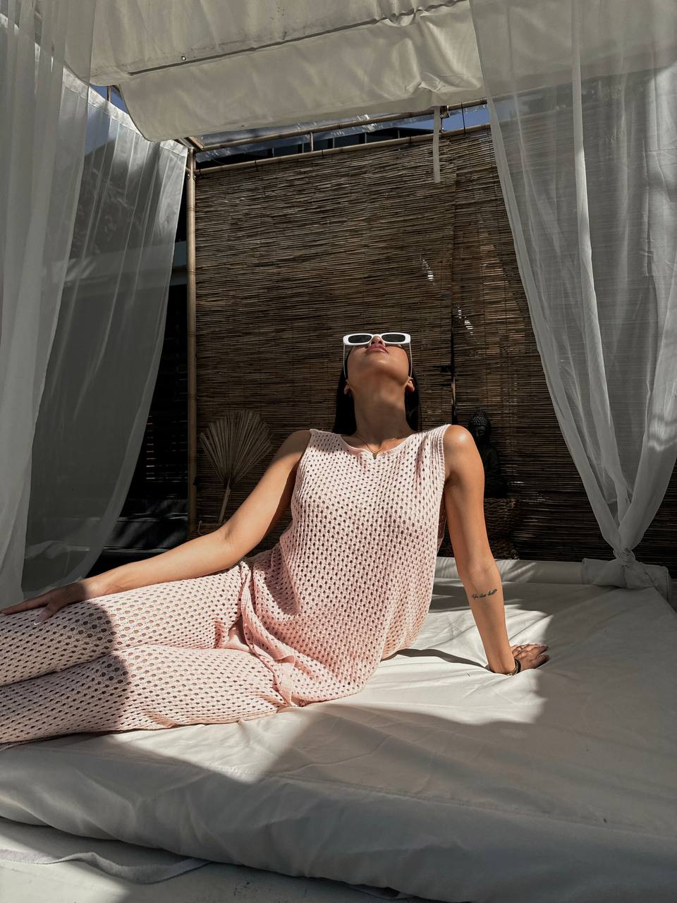 Woman in a pink dress lying on a bed with white curtains and wooden wall in the background