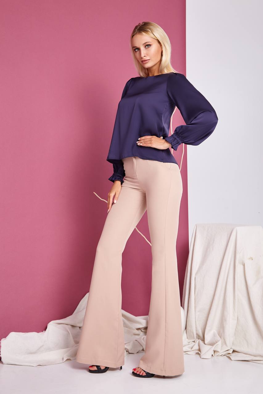 Woman wearing a purple top and beige pants against a pink and white background