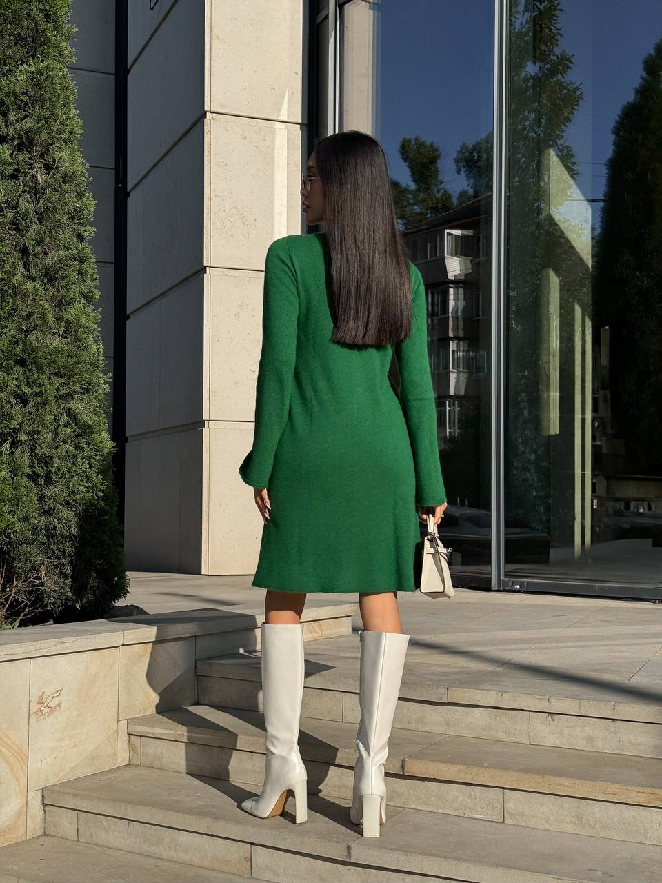 Woman in a green dress and white knee-high boots standing on steps outside a modern building.
