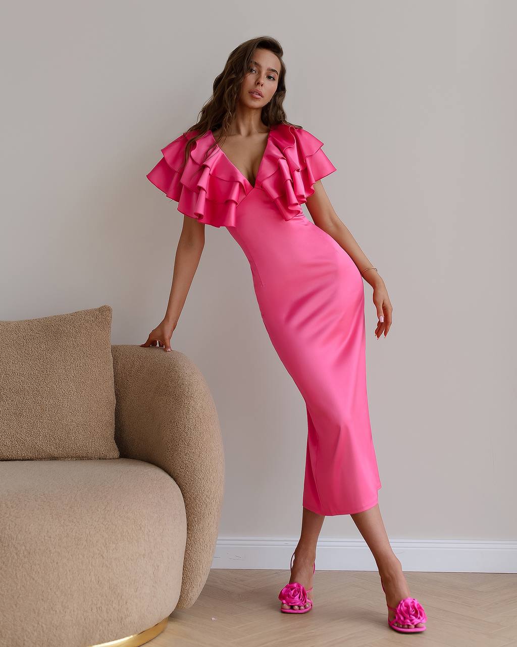 Woman wearing a pink dress with ruffled sleeves in a room with a beige sofa.