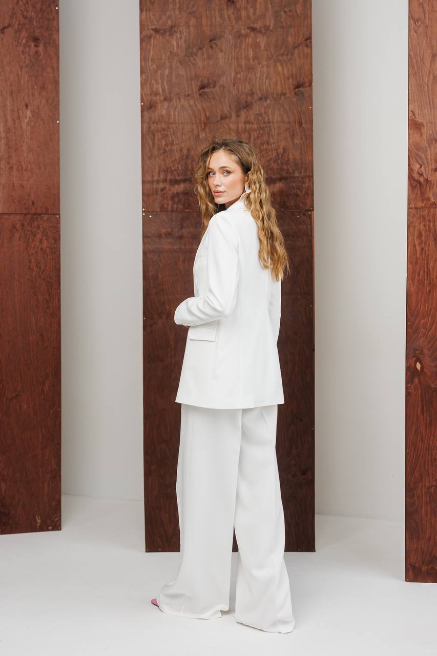 Woman in a white suit standing against a modern architectural background with columns.