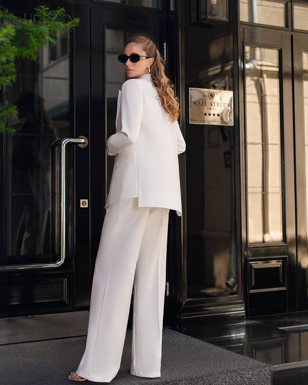 Woman in a white outfit standing outside a building with a sign.
