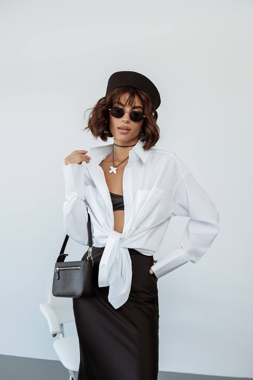 Woman wearing a white shirt with a black tie, black skirt, and sunglasses against a white background