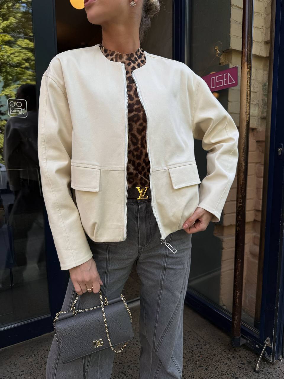 Person wearing a cream jacket, leopard print top, and gray jeans holding a gray handbag.
