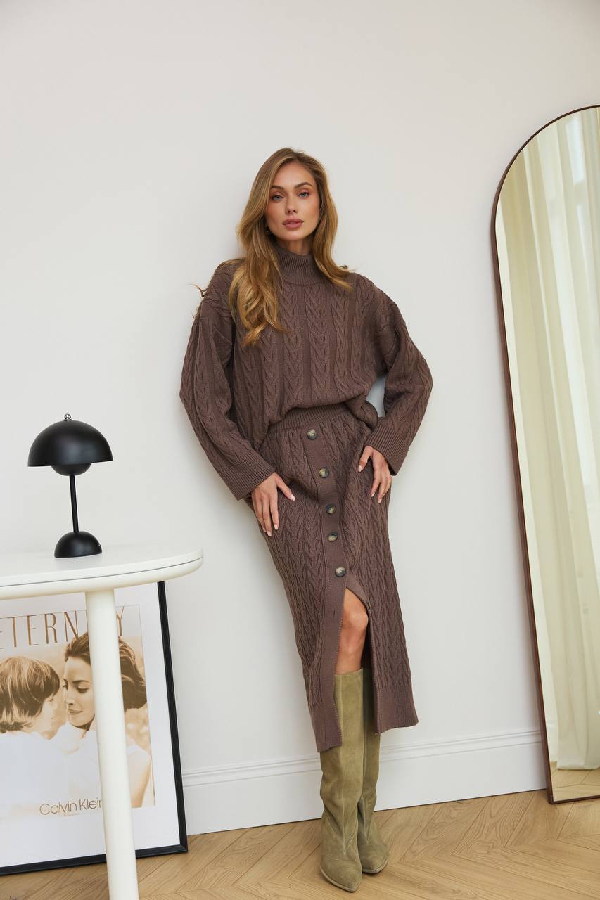 Woman in a brown knit outfit standing in a room with a mirror and decor.