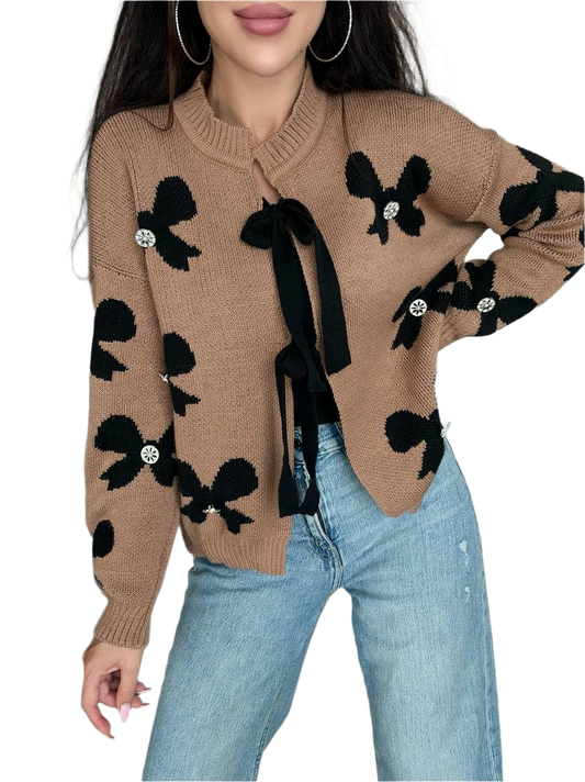 Beige sweater with black bow patterns worn by a person on a white background