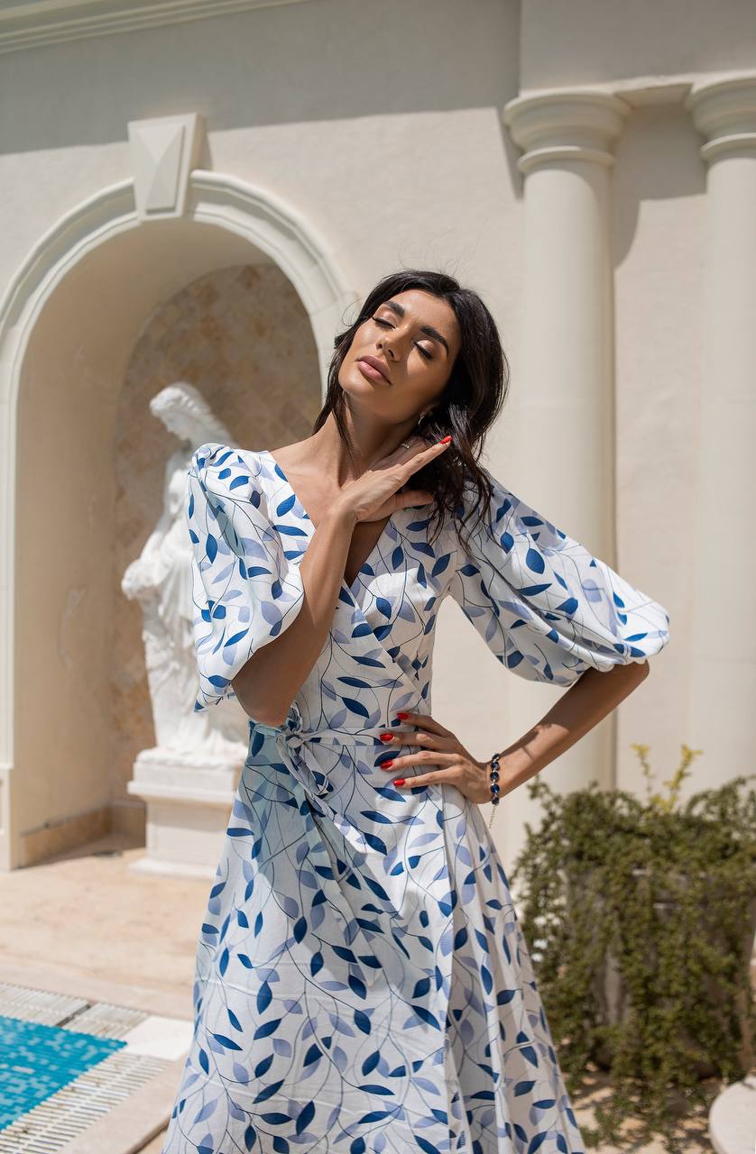 Woman in a white dress with blue floral pattern standing in an elegant outdoor setting.