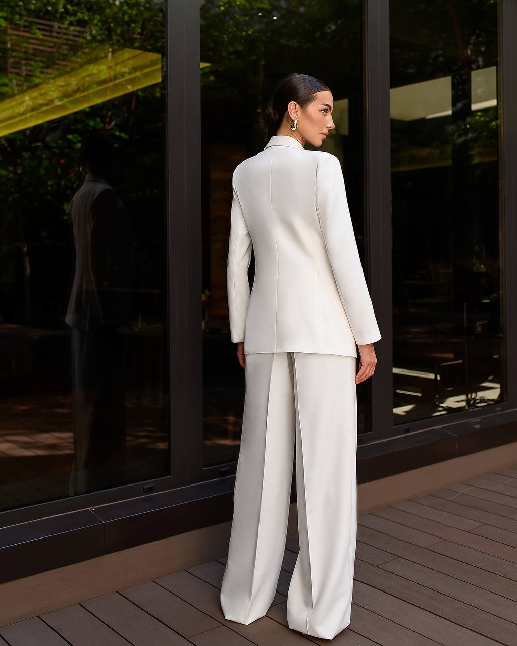 Woman in a white suit standing in front of a reflective glass building.
