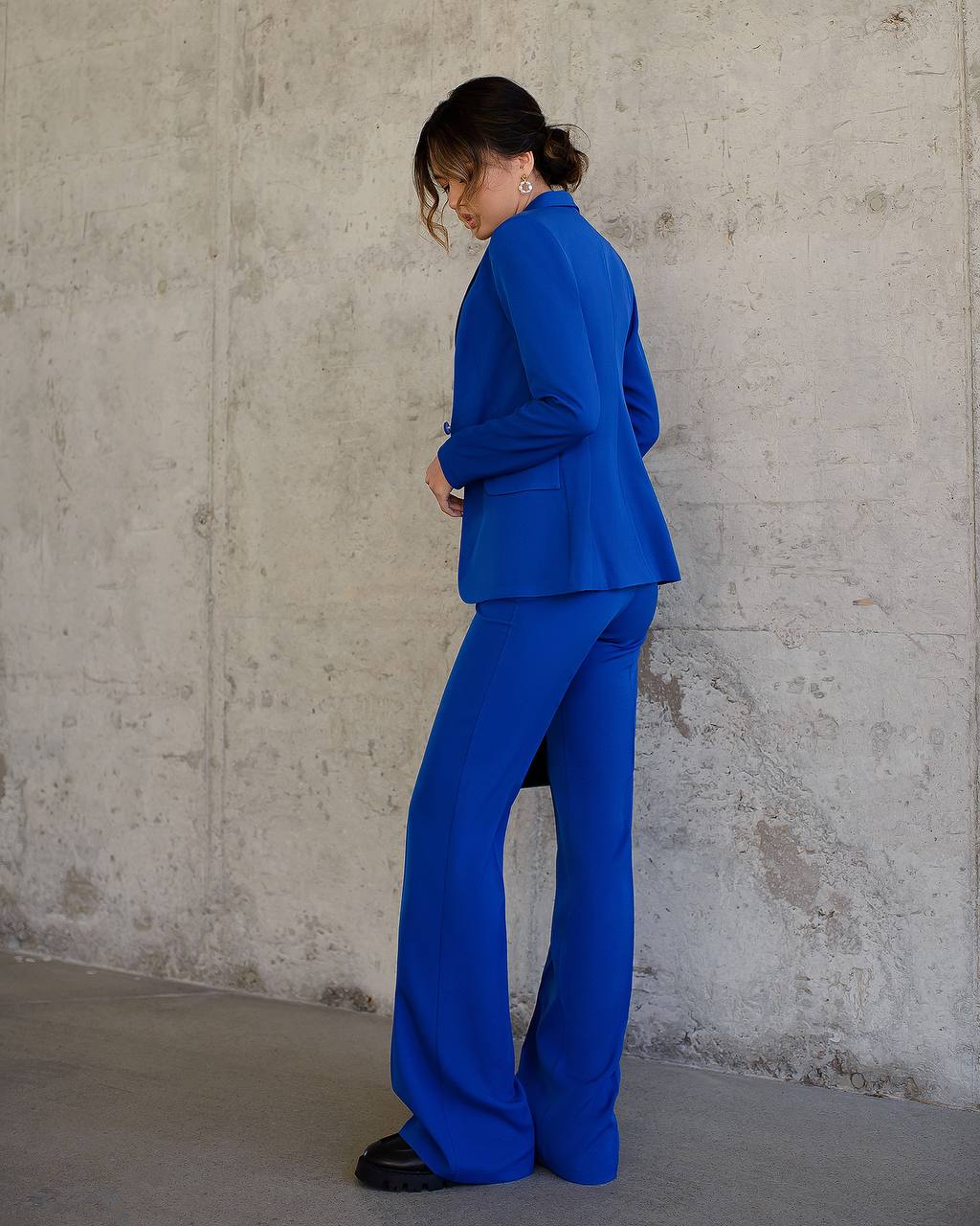 Person wearing a blue suit standing against a concrete wall.