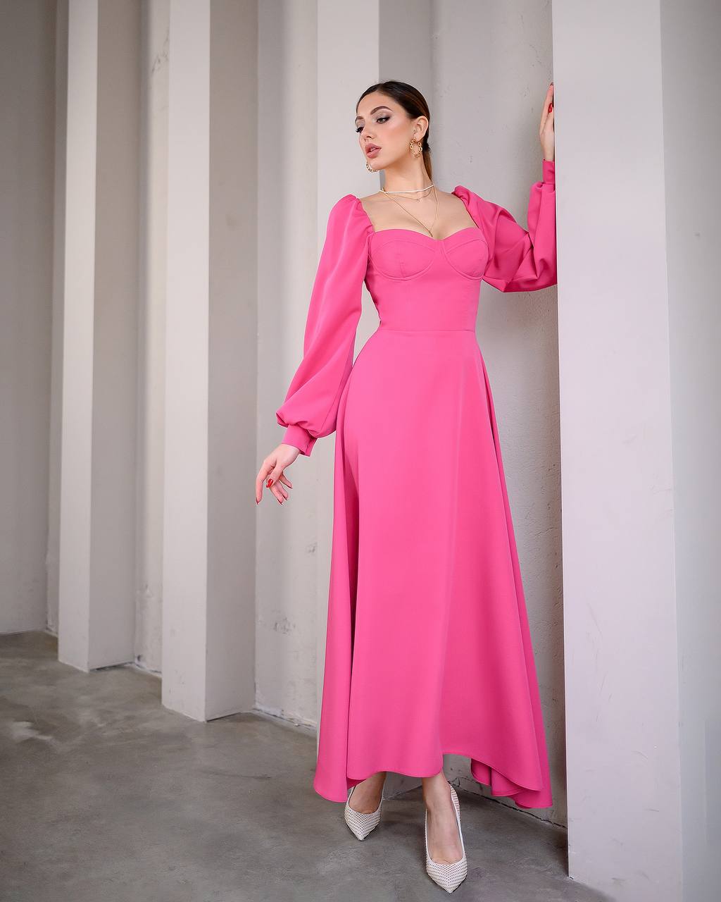 Woman wearing a pink evening gown standing against a plain wall.