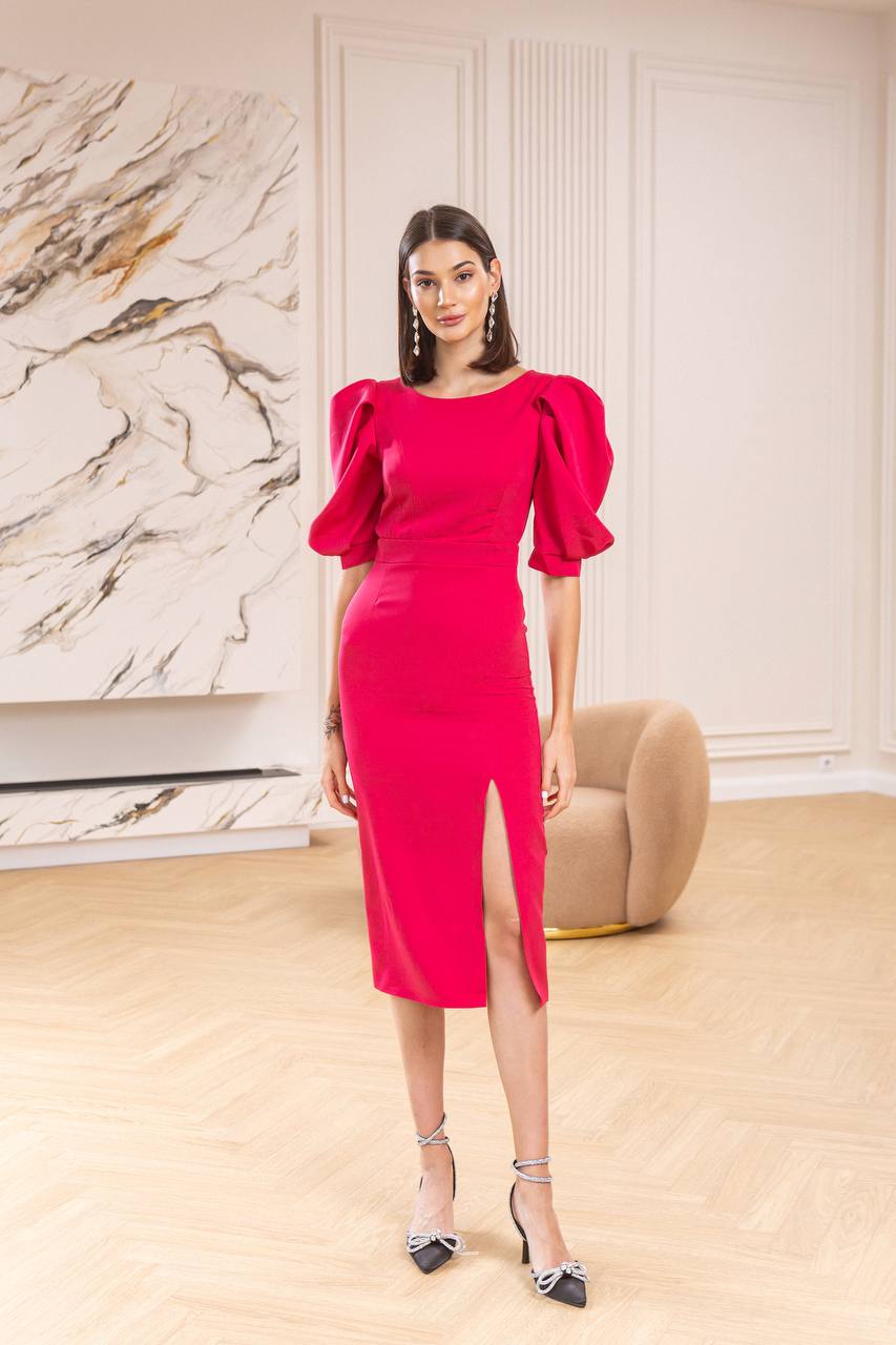 Woman in a bright pink dress standing in a room with marble walls and a beige chair.