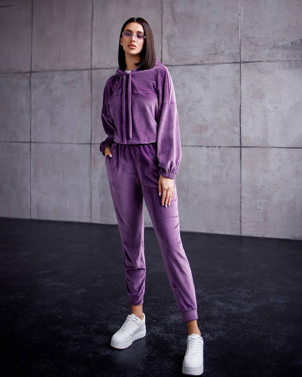 Woman wearing a purple tracksuit against a gray wall.