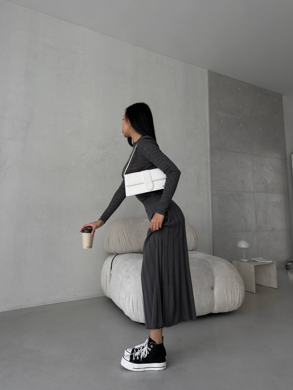 Person holding a white bag and a coffee cup in a minimalistic room.