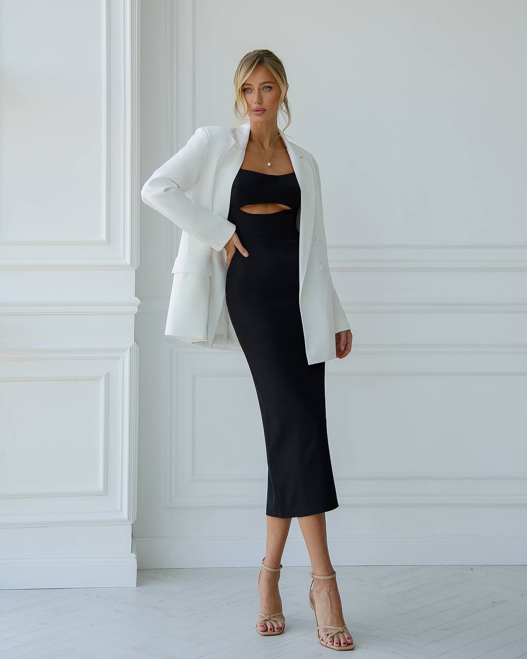 Woman wearing a black dress and white blazer against a white wall
