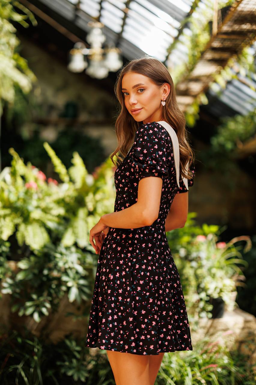 Woman in a black floral dress standing in a garden setting