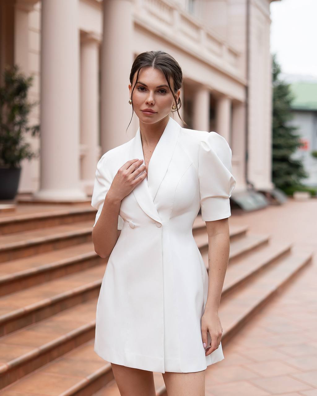 Woman in a white dress standing outdoors with classical architecture in the background